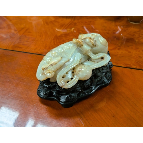 564 - A Chinese carved mutton fat jade lion, curled, with ebonised pierced stand with cloud decoration, li...
