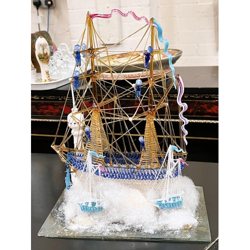 477 - A Victorian blown glass model of a two masted brig with sailors on rigging with small boats moored w... 