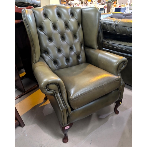 894 - An antique green wing back Chesterfield deeply button back arm chair with stool 