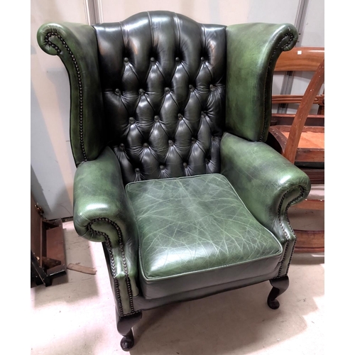 943 - An antique green high wing back chesterfield chair with button back