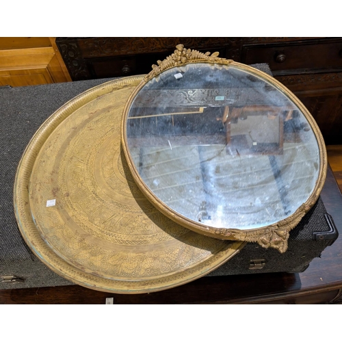 1023 - An Eastern occasional table with brass tray top and folding legs; an oval mirror with ormolu mounts.