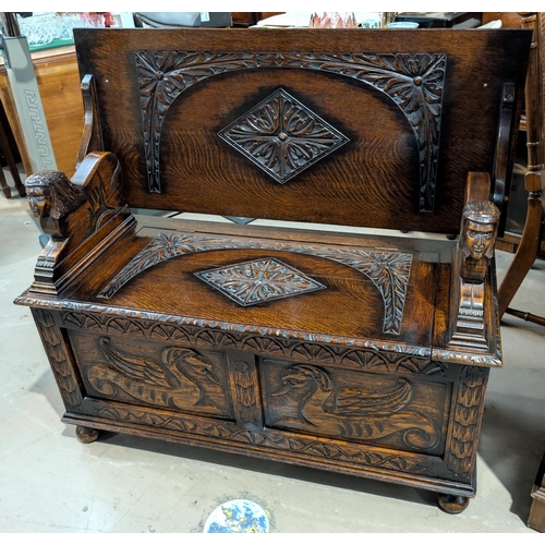 847 - A carved oak monks bench with hinged storage and sphynx supports.