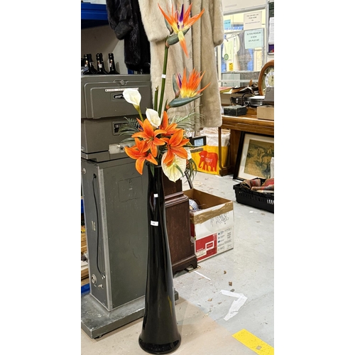 63 - A tall, floor standing glass vase with floral displays.No bids sold with lot 64