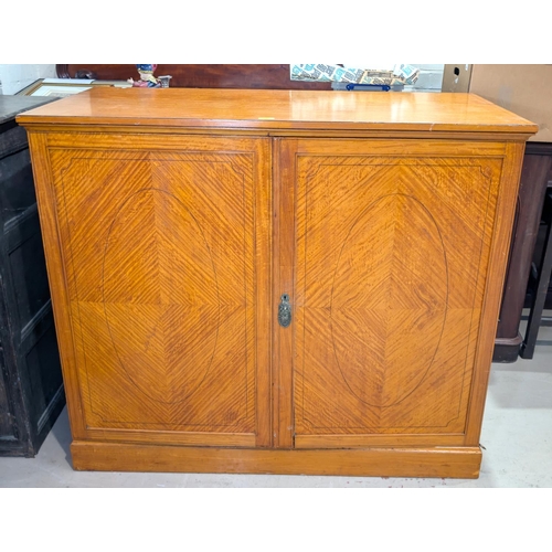 1059 - An early 20th century quarter veneered satinwood low press cupboard with twin doors enclosing slidin... 