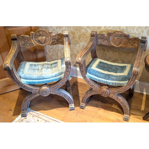 920 - A pair of Medieval style 'W' shaped chairs with carved armorial details.