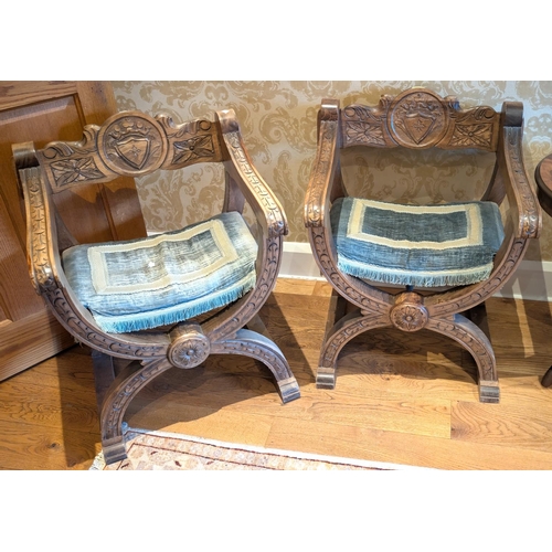 920 - A pair of Medieval style 'W' shaped chairs with carved armorial details.