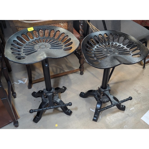 1094 - A pair of tractor seat rise and fall bar stools with four splay feet and twisted foot rest.