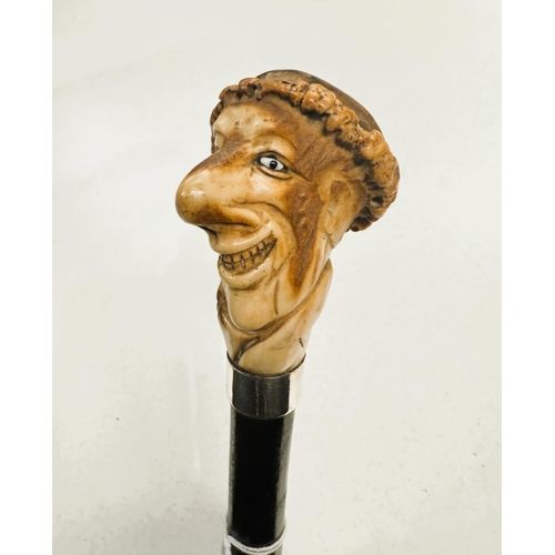 178 - An ebonised walking stick with carved antler finial in the form of a caricature head, 88cm.