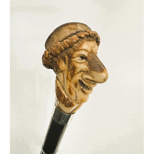 178 - An ebonised walking stick with carved antler finial in the form of a caricature head, 88cm.