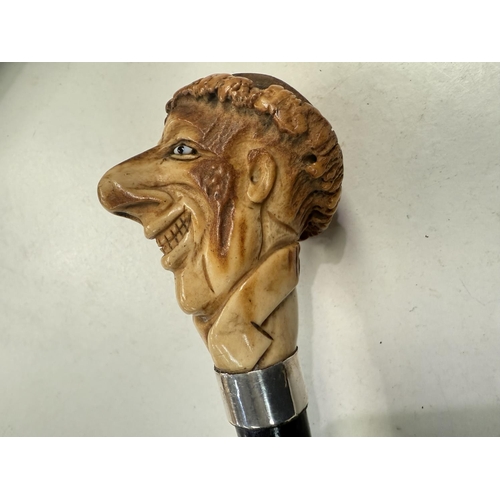 178 - An ebonised walking stick with carved antler finial in the form of a caricature head, 88cm.