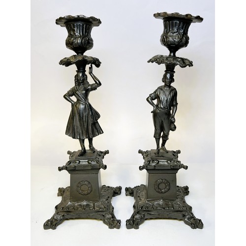 14 - A pair of cast metal candle sticks with male and female column with squared base and a small spelter... 