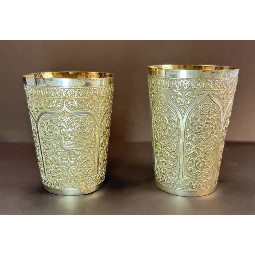 763 - A matched pair of early 20th century Indian white metal beakers with scrolling decoration 12.7oz.