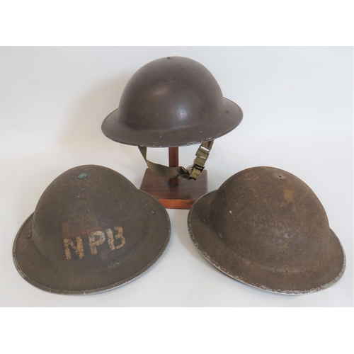 Three British Steel Helmets
consisting brown painted shell.  Black treated linen liner.  Frame with faint date.  Cruciform rubber crown pad.  Sprung side webbing chinstrap ... Khaki brown painted example.  The front stencilled "NPB".  Liner broken and loose.  Sprung side webbing chinstrap ... MKII steel helmet shell (rusted).  Lining absent.  Sprung sided webbing chinstrap.  3 items.