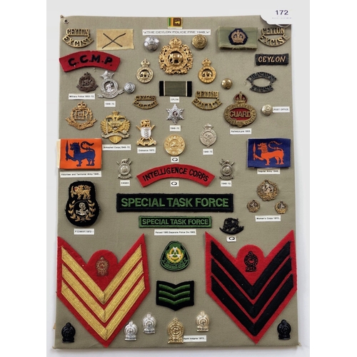 172 - Ceylon Police 48 items of insignia.  Board with good display of metal and cloth badges and buttons. ... 