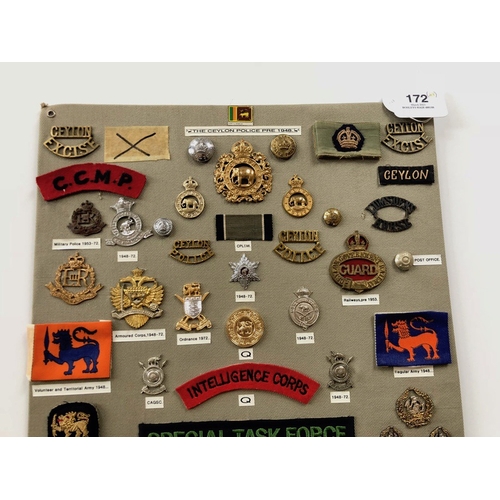 172 - Ceylon Police 48 items of insignia.  Board with good display of metal and cloth badges and buttons. ... 