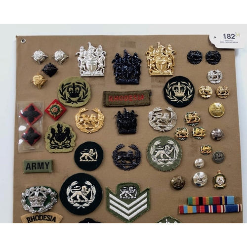 182 - Rhodesia  55 items of insignia.  Board with good display of metal and cloth badges and buttons. Most... 