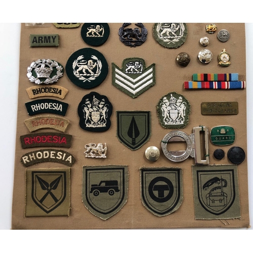 182 - Rhodesia  55 items of insignia.  Board with good display of metal and cloth badges and buttons. Most... 