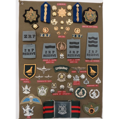 Zimbabwe Army & Police - 45 Items Of Insignia
display board with good tabulated display of metal and cloth badges including Parachute Reg ... Commando Bn ... Greys Scouts ... ZRP Reserve ... Zimbabwe belt buckle.  45 items.  Bob Betts collection.  