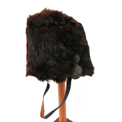 Victorian Royal Artillery Officer's Busby
dark brown fur body.  Scarlet felt side and crown bag.  The left side with brass Victorian crown Artillery flaming grenade with rear plume holder.  Cream leather and maroon sweatband.  Black patent leather chinstrap.  Some fur loss and internal panel of crown loose.  