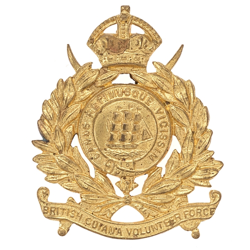 Badge. West Indies. British Guiana Volunteer Force cap badge circa 1948-52.  Good scarce British made die-stamped brass example. Set on crossed swords crowned laurel sprays on title scroll; centrally a galleon in motto strap    Loops  VGC