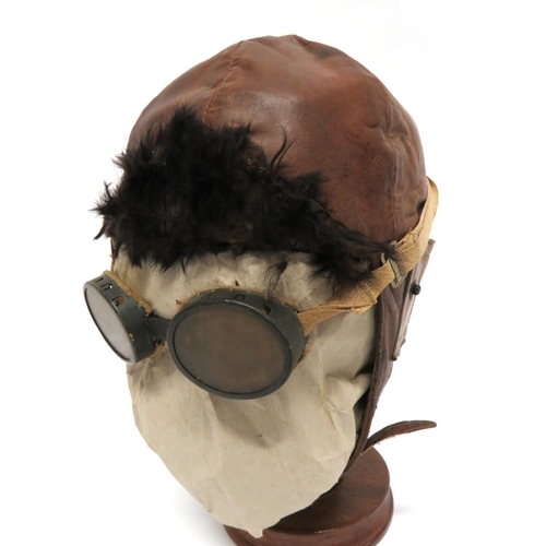 WW1/1920's Flying/Driving Helmet
brown leather, multi pad helmet.  Fold up, fur covered, front peak.  Side, roll up ear flaps.  Leather chinstrap.  Blanket lining.  Together with a pair of WW1 pattern flying goggles. Tinted, oval lenses.  Grey painted, brass frames.  Elasticated strap.  Complete on a display stand.  