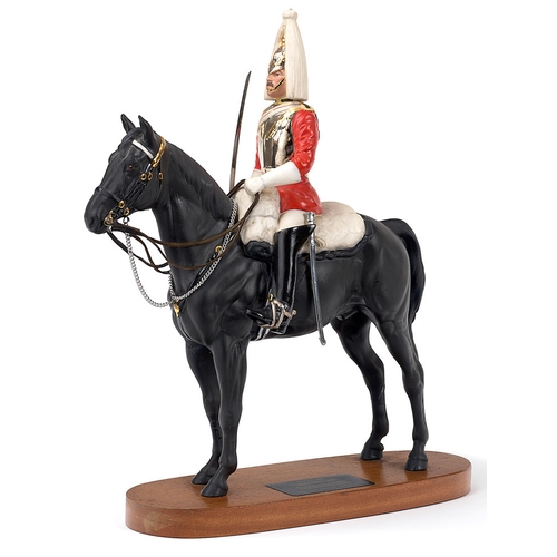 Beswick China figure of a Mounted Trooper of the Life Guards.  This finely executed ceramic figure displays a Trooper of the Regiment in Review Order. His right hand holds the State Pattern Sword at the Present. Complete with nickel chain and leather reins, tightly held by the left hand. Mounted onto the original polished wooden base with a plaque bearing the details. Height 15 inches. One horse ear repaired Good detail and colour.        Viewing Recommended