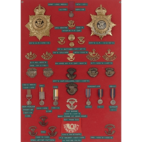 305 - Somerset Light Infantry helmet plates, badges, shoulder titles etc.  Board with good display of appr... 