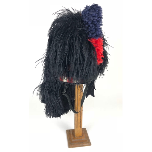 Scots Guards Piper’s Feather Bonnet  A good clean example of the black feather bonnet with four side tails.  Lower red, white and black checkered band, with three rear tails. Complete with Scots Guards pipers plume, the interior with simulated leather sweatband, cloth lining and chinstrap. Overall clean condition, no badge.