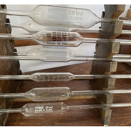 311 - Scientific glass pipettes, mainly Pyrex seated on a wooden rack together with a conical flask (2)