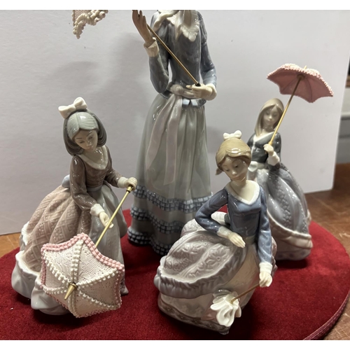 369 - 4 Lladro ladies on a red velvet stand all with umbrellas