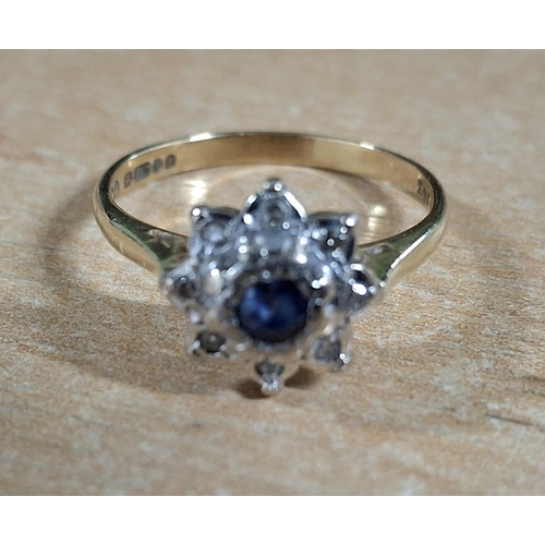 19 - Hallmarked 18ct yellow gold flower ring with large, raised round cut Sapphire flanked by smaller, il... 