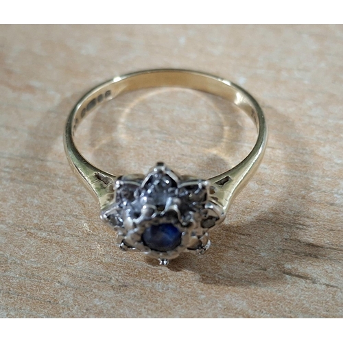 19 - Hallmarked 18ct yellow gold flower ring with large, raised round cut Sapphire flanked by smaller, il... 