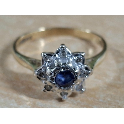 55 - Hallmarked 18ct yellow gold flower ring with large, raised round cut Sapphire flanked by smaller, il... 
