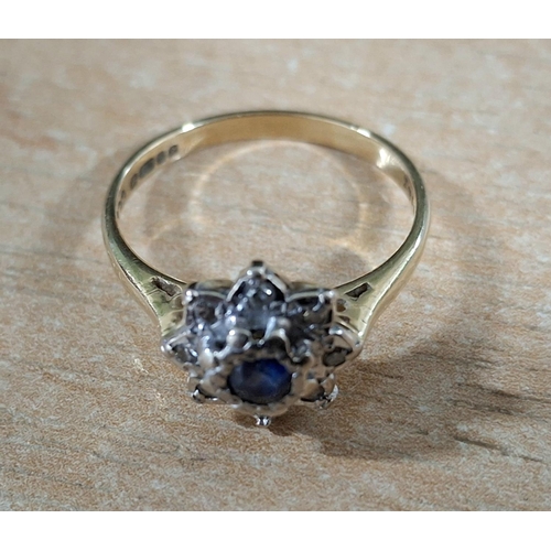 55 - Hallmarked 18ct yellow gold flower ring with large, raised round cut Sapphire flanked by smaller, il... 