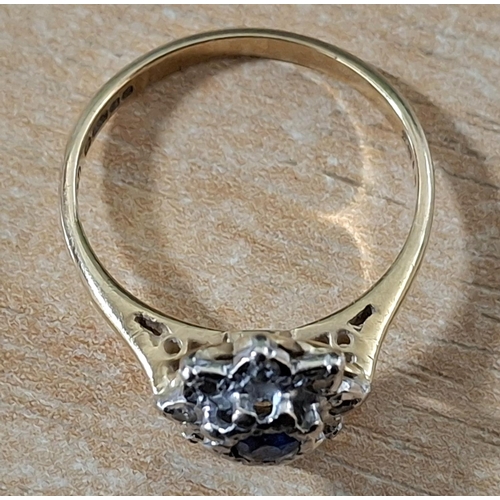 55 - Hallmarked 18ct yellow gold flower ring with large, raised round cut Sapphire flanked by smaller, il... 
