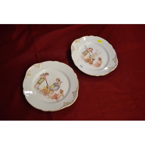 358 - 2 Putto hand-decorated plates. 1 with staple repairs. W25.5cm