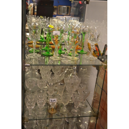 409 - Glassware & crystal over 2 shelves inc. Green stemmed wine glasses & etched crystal