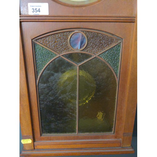 354 - Mahogany cased wall clock with brass face and brass pendulum and features a stained glass viewing pa... 