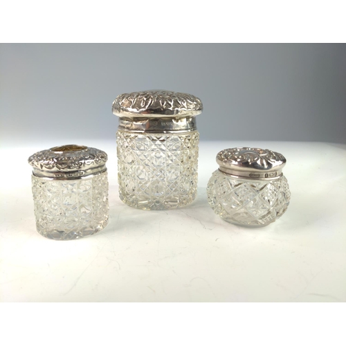 391 - Ten embossed silver topped glass vanity jars, various makers and dates