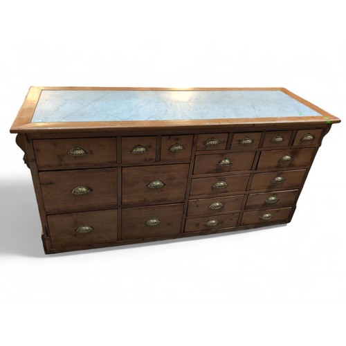 575 - An early C20 Apothecary / Chemists counter. With 19 drawers with brass cup handles, and inset marble... 