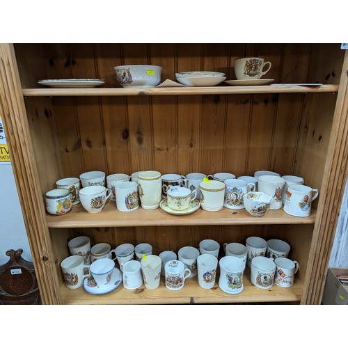 679 - Commemorative ware over three shelves, inc. Clarice Cliff Coronation teacup and saucer, Royal Crown ... 