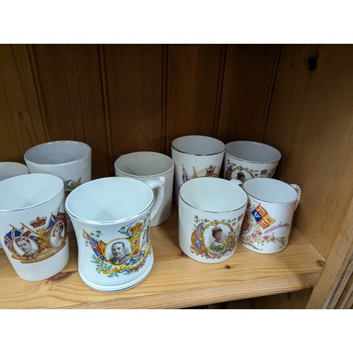 679 - Commemorative ware over three shelves, inc. Clarice Cliff Coronation teacup and saucer, Royal Crown ... 