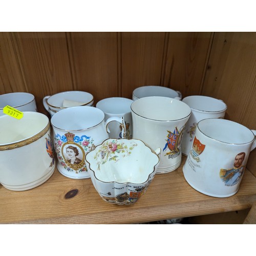 679 - Commemorative ware over three shelves, inc. Clarice Cliff Coronation teacup and saucer, Royal Crown ... 