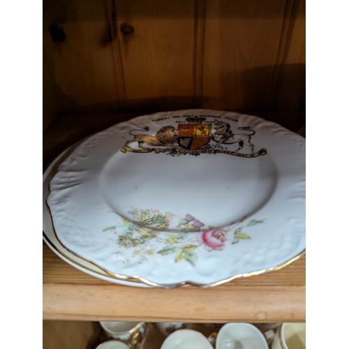 679 - Commemorative ware over three shelves, inc. Clarice Cliff Coronation teacup and saucer, Royal Crown ... 