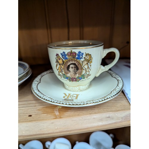 679 - Commemorative ware over three shelves, inc. Clarice Cliff Coronation teacup and saucer, Royal Crown ... 