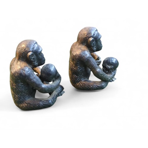 410 - 2 metal chimps holding human skulls. H6cm.