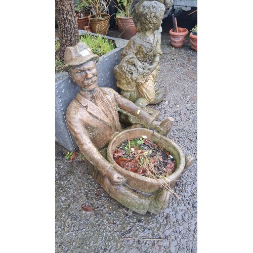 87 - A figural cast stone garden planter modelled as a seated gentleman in hat and suit, holding a circul... 