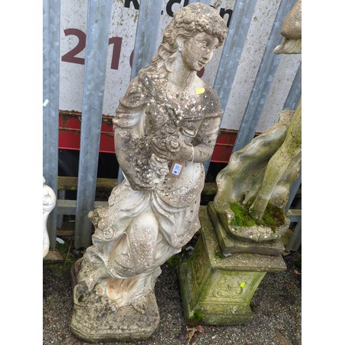 A cast stone garden statue of a maiden in classical drapery, modelled standing with a floral garland and flower-filled apron, on an integral shaped plinth base.