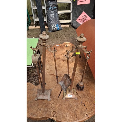 250E - A pair of brass and steel companion sets, each with baluster finial above pierced yoke, fitted with ... 
