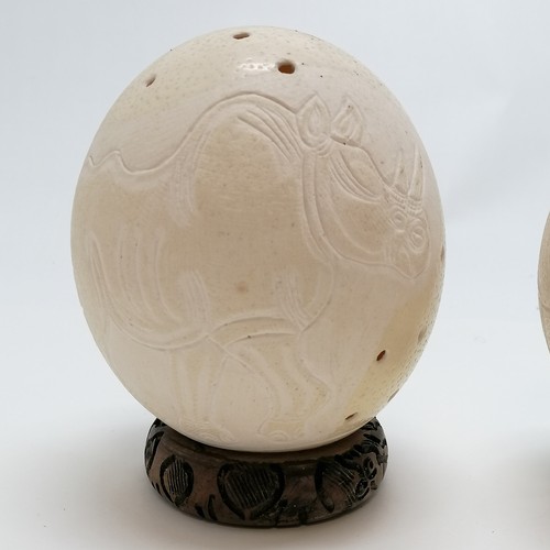 55 - 2 x ostrich eggs carved with rhino & elephant signed Musa - both have wooden stands